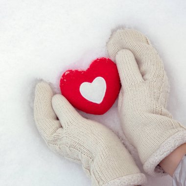 winter love background, hands in knitted mittens hold a red heart on fresh snow