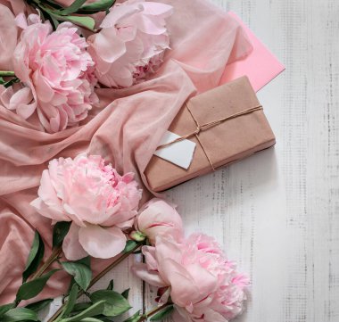 Taze pembe şakayık çiçekleri ve ahşap bir masada hediye kutusu. Üst görünüm bayram karşılama arkaplanı