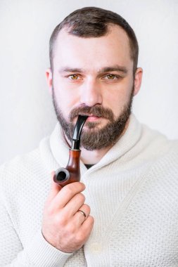 Hafif hırkalı, sakallı ve bıyıklı gülümseyen bir beyefendi pipo tutuyor ve sigara içiyor, şık, modaya uygun bir adam.