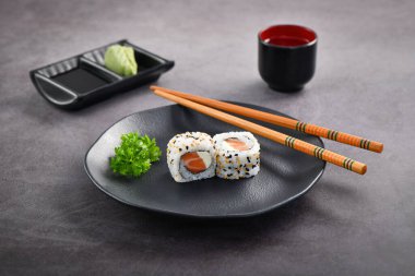 Somon ve krem peynirli suşi çifti koyu tabakta servis ediliyor. Stüdyo çekimi.