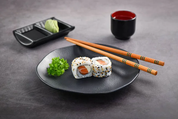 Salmon and Cream Cheese sushi couple served on dark dish. Studio shoot.