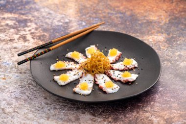 Taze ahtapot dilimleri, siyah tabakta balık yumurtasıyla servis edilir.. 