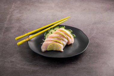 Beyaz balıklı saşimi siyah tabakta dilimler. Stüdyo çekimi arka planda.