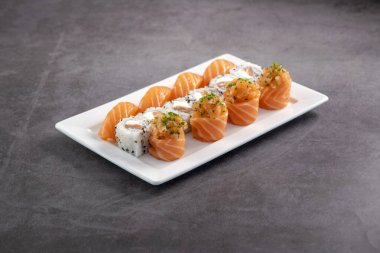 Taze suşi karışımı. Beyaz tabakta servis edilen farklı somon suşisi çeşitleri. Kapalı arkaplanda stüdyo çekimi.