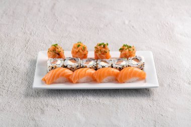 Taze suşi karışımı. Beyaz tabakta servis edilen farklı somon suşisi çeşitleri. Kapalı arkaplanda stüdyo çekimi.