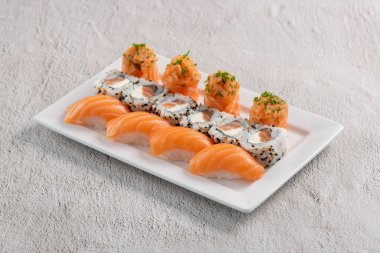 Taze suşi karışımı. Beyaz tabakta servis edilen farklı somon suşisi çeşitleri. Kapalı arkaplanda stüdyo çekimi.