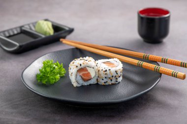 Somon ve krem peynirli suşi çifti koyu tabakta servis ediliyor. Stüdyo çekimi.