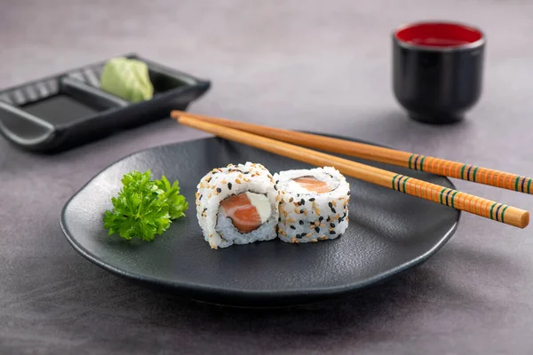 Somon ve krem peynirli suşi çifti koyu tabakta servis ediliyor. Stüdyo çekimi.