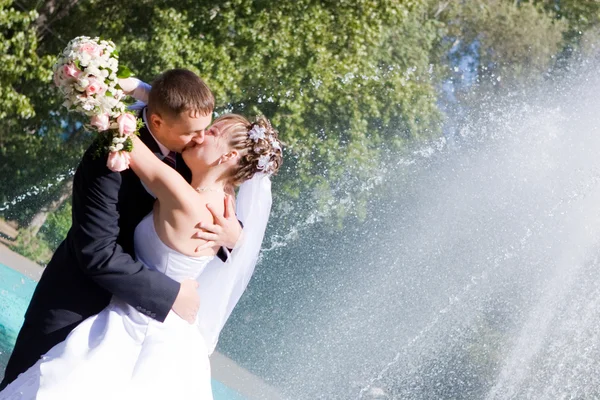 Una sposa e uno sposo si baciano vicino alla fontana — Foto Stock