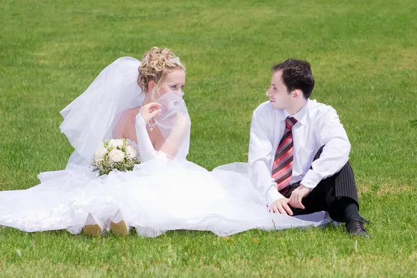 Uma noiva e um noivo olhando um para o outro na grama — Fotografia de Stock