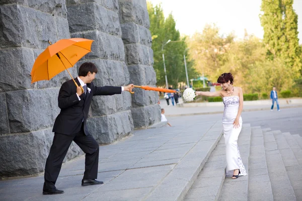 Bruid en bruidegom met oranje paraplu 's — Stockfoto