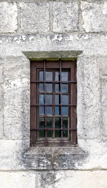 old rusty window with bars on a stone wall
