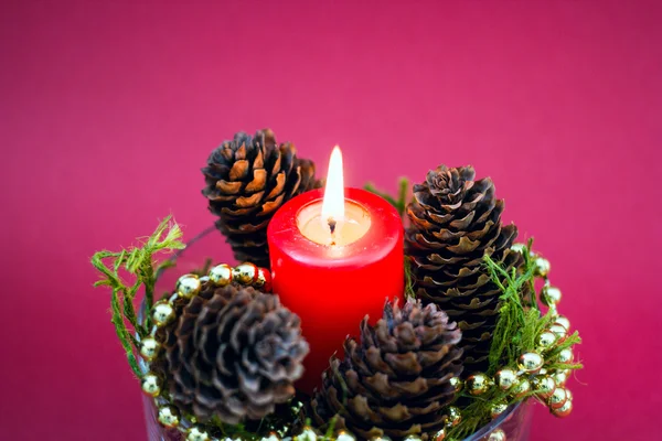 Composición decorativa de Navidad de vela roja, conos de pino sobre fondo rojo — Foto de Stock