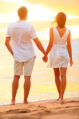 Young couple holding hands at beach sunset clipart