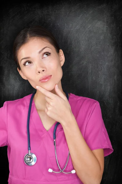 Female medical doctor nurse thinking by blackboard — Stock Photo, Image