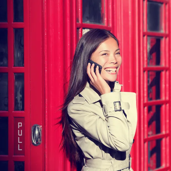 Mulher no telefone inteligente pela cabine de telefone vermelho — Fotografia de Stock