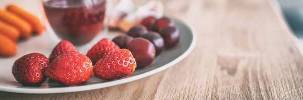 Frutas orgánicas y fresas frescas y uvas en mesa de madera en casa o restaurante de brunch. Desayuno snack plato desintoxicación saludable fresa, uvas rojas, naranjas, zanahorias banner panorama —  Fotos de Stock