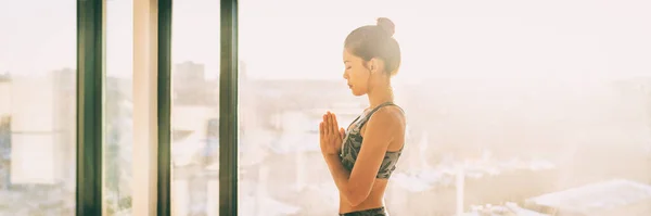 Yoga meditasyonu yapan sağlıklı kız spor salonunda sabah güneşinde dua ediyor. Yoga öğretmeni namaste Asyalı kadın evinde güneşli panorama arka planında egzersiz yapıyor. — Stok fotoğraf