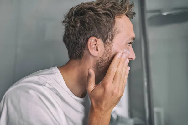 Huidverzorging jongeman zet gezichtscrème voor gezichtsbehandeling acne behandeling in huis badkamer. Mannen schoonheid huidverzorging levensstijl — Stockfoto