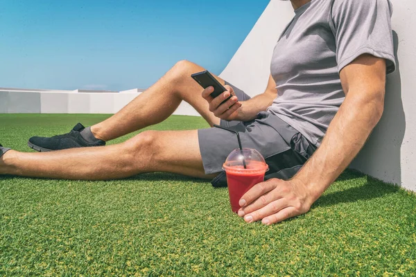 Hombre activo saludable usando teléfono bebiendo jugo de remolacha smoothie bebida para llevar taza en verano gimnasio al aire libre fondo del parque. Primer plano de teléfono inteligente y vidrio de plástico —  Fotos de Stock