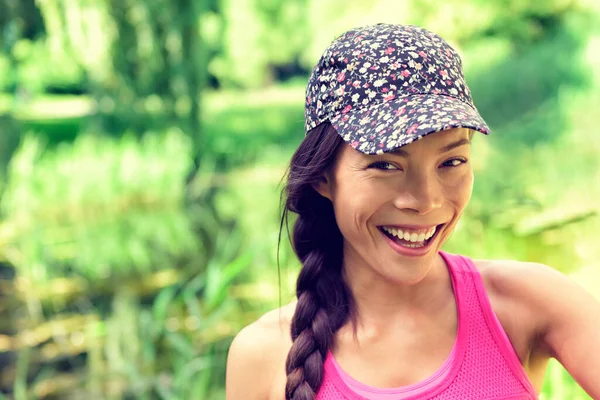 Junge glückliche gesunde asiatische Mädchen lächeln in die Kamera. Chinesisch-kaukasischen multirassischen Frau tragen Modekappe und Haarzopf im Sommer Park grünen Gras Hintergrund. Natürliche Schönheit. — Stockfoto