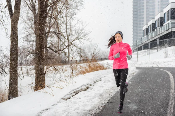 Téli futó ázsiai lány visel hideg időjárás ruházat külső gyakorlása hóvihar hóesés során téli edzés szabadban a város utcájában. Fitness nő gyakorlása. — Stock Fotó
