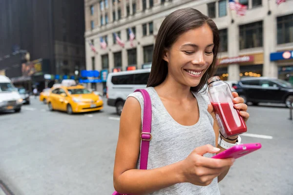 Urban city modern Asian girl using phone app drinking healthy fruit vegetable juice smoothie walking on Manhattan street New York, États-Unis. Happy jeune adulte mode de vie sain. — Photo