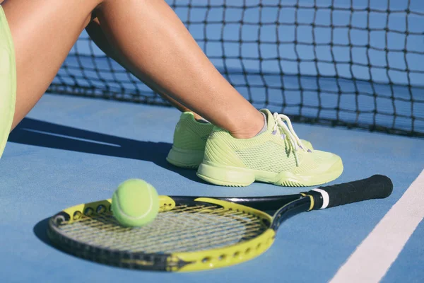 Tennisspelare kvinna ben och fötter bär tennisskor tränare. Mode gul aktiva kläder outfit på blå utomhus hård domstol. Närbild av ben och fötter, racket och boll — Stockfoto