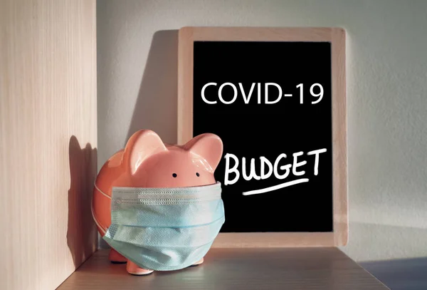 Coronavirus-Pandemie Wirtschaftskrise Tafel. Sparschwein mit chirurgischer Gesichtsmaske und Budget Board. Finanzkrise, Bankwesen während COVID-19 — Stockfoto