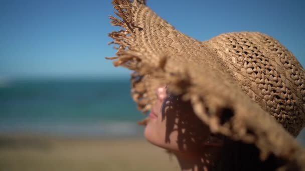 Nő strand szépség portré videó. Egy hölgy napvédő szalmakalapot visel a strandon. Nyári utazás gyönyörű fiatal biracial lány pihentető mosoly csukott szemmel. — Stock videók