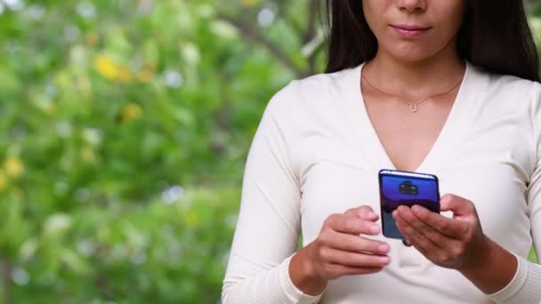 Mujer joven sosteniendo el teléfono usando la aplicación bancaria u otra aplicación que se desplaza escribiendo y deslizando en el teléfono móvil en línea — Vídeos de Stock