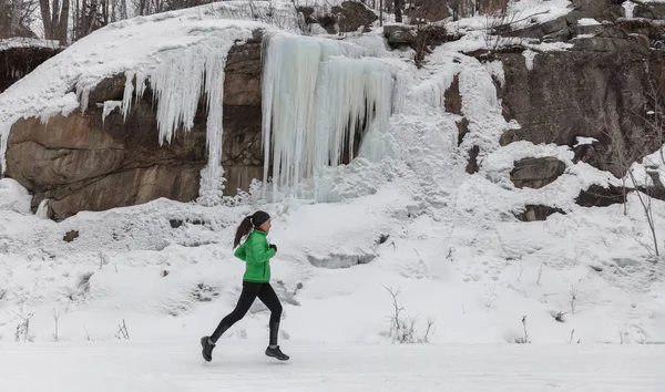 冬跑女运动员在雪道上跑步，在寒冷的天气下在室外训练有氧运动。亚洲女赛跑选手穿着紧身裤和活动外套在外面锻炼 — 图库照片