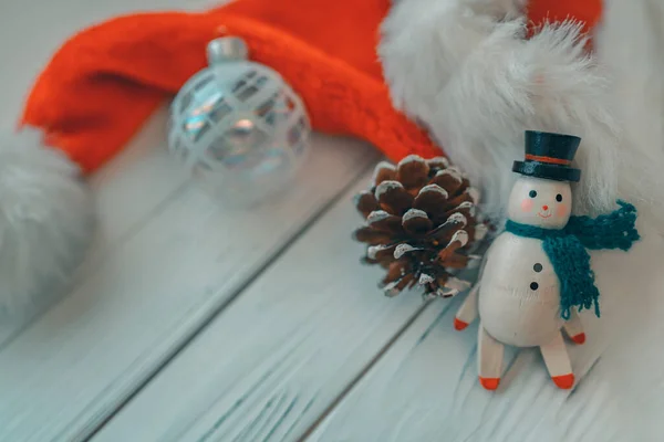 Weihnachten hölzerner Schneemann weiß Holz Hintergrund mit Miniatur-Vintage-Spielzeug, Tannenzapfen, Glaskugelornament und Weihnachtsmütze für die Weihnachtsfeiertage — Stockfoto