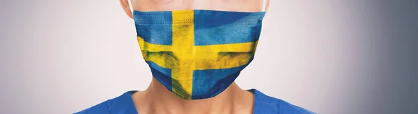 Suécia bandeira impressão em sueco médico enfermeiro homem ou mulher rosto PPE no fundo cinza bandeira panorâmica. Conceito de coronavírus — Fotografia de Stock