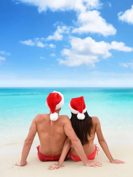 Boże Narodzenie wakacje na plaży para relaks siedzi na białym piasku patrząc na turkusowy widok na ocean w tropikalnym celu podróży. Para z tyłu razem opalać się w kapeluszu Mikołaja. — Zdjęcie stockowe