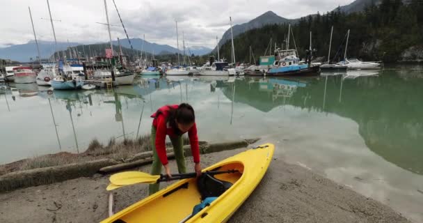 女人带着皮划艇去准备皮划艇。俯瞰斯卡拉米什港口、船只和山脉。加拿大不列颠哥伦比亚省 — 图库视频影像