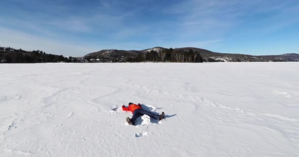 Девушка делает снежного ангела на замерзшем озере, развлекаясь в зимнем пейзаже чудес природы, Молодая женщина делает снежного ангела — стоковое видео