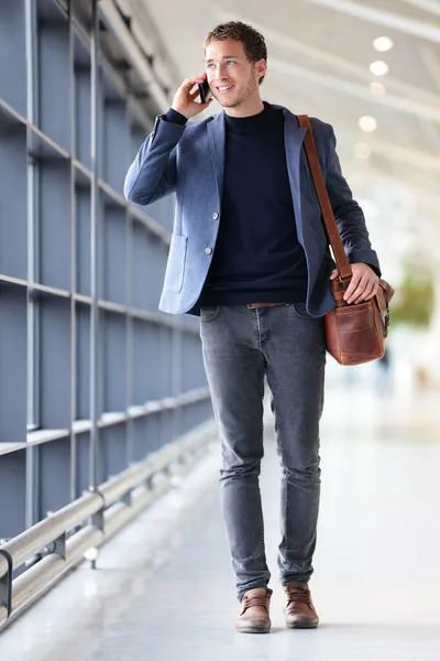 Homme d'affaires urbain parlant sur un téléphone intelligent voyageant à l'intérieur de l'aéroport. Jeune homme d'affaires décontracté portant une veste de costume et un sac à bandoulière. Beau modèle masculin dans la vingtaine . — Photo