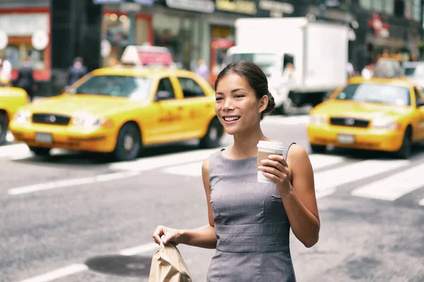 Donna d'affari asiatica di New York che cammina verso il lavoro con la borsa del pranzo al mattino mentre beve una tazza di caffè per strada con i taxi gialli sullo sfondo. Persone stile di vita pendolare. — Foto Stock