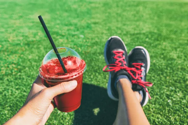 Chica bebiendo remolacha roja o batido de frutas taza de plástico durante el entrenamiento de fitness. Jugo de desintoxicación saludable mujer sosteniendo zapatos para correr de ducha de bebida en foto selfie de alimentos. Deporte estilo de vida activo —  Fotos de Stock