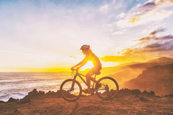 Bicicleta de montaña ciclista chica montando bicicleta MTB en el sendero de la costa contra la puesta de sol. Silueta de mujer haciendo deportes al aire libre. Estilo de vida saludable y activo. — Foto de Stock