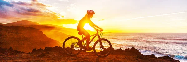 Mountain biking cyclist riding bike on coast trail against sunset. Silhouetter of woman doing sports outdoors banner panorama. Active lifestyle. — Stock Photo, Image