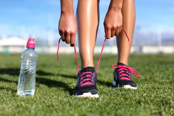 健康的なアクティブライフスタイルの概念のトレーニングを開始-ランナーの女の子は水ボトルでランニングシューズを結ぶ草の上に行使する準備を取得. — ストック写真