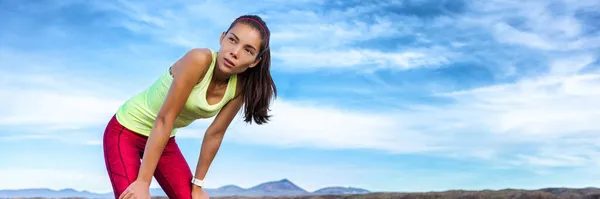 Exercise tired runner girl taking a break breathing during jogging training workout outdoor on desert trail. Asian woman sweating in summer heat. banner panoramic header with copy space on sky. — Stock Photo, Image