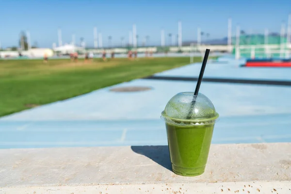 Bebida de jugo de desintoxicación de batido verde en el estadio deportivo al aire libre para atletas corredores en pista de atletismo azul. Dieta saludable batido de proteínas para deportistas. — Foto de Stock