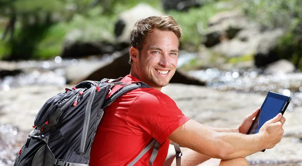 Tablet computer man wandelaar wandelen in de VS bos buiten met behulp van reizen app of kaart op draagbare apparaat tijdens de wandeling. Blanke mannelijke wandelaar ontspannen op een zomerse dag aan de rivier. — Stockfoto