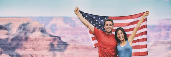 悬挂大峡谷旗帜背景下的美国国旗的美国游客。年轻的种族间快乐的夫妇在暑假里欢呼. — 图库照片