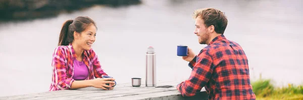 Camping happy couple drinking coffee on morning breakfast table at campsite enjoying summer tourism holidays. Asian tourist woman with man, outdoor. — Stock Photo, Image