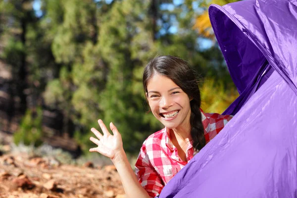 Chica que acampa saludando desde la tienda de campaña exterior - aventura de verano de viajes forestales. feliz asiático mujer tener divertido. —  Fotos de Stock