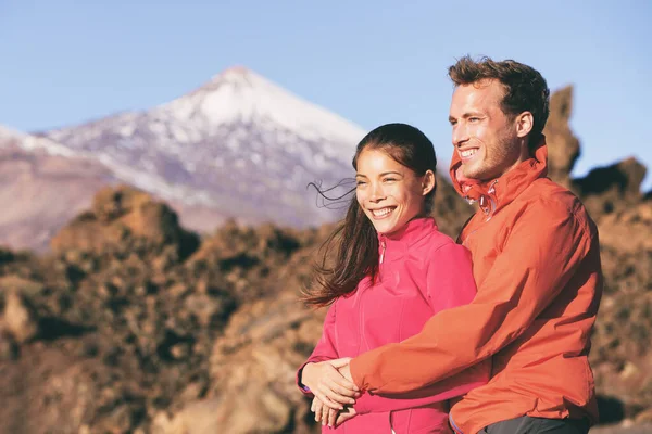 Joyeux couple de randonnée relaxant dans la nature de montagne étreignant. Amateurs interraciaux randonneurs souriants, femme asiatique, homme caucasien portant des vestes d'hiver pour le printemps froid. Style de vie en plein air. — Photo